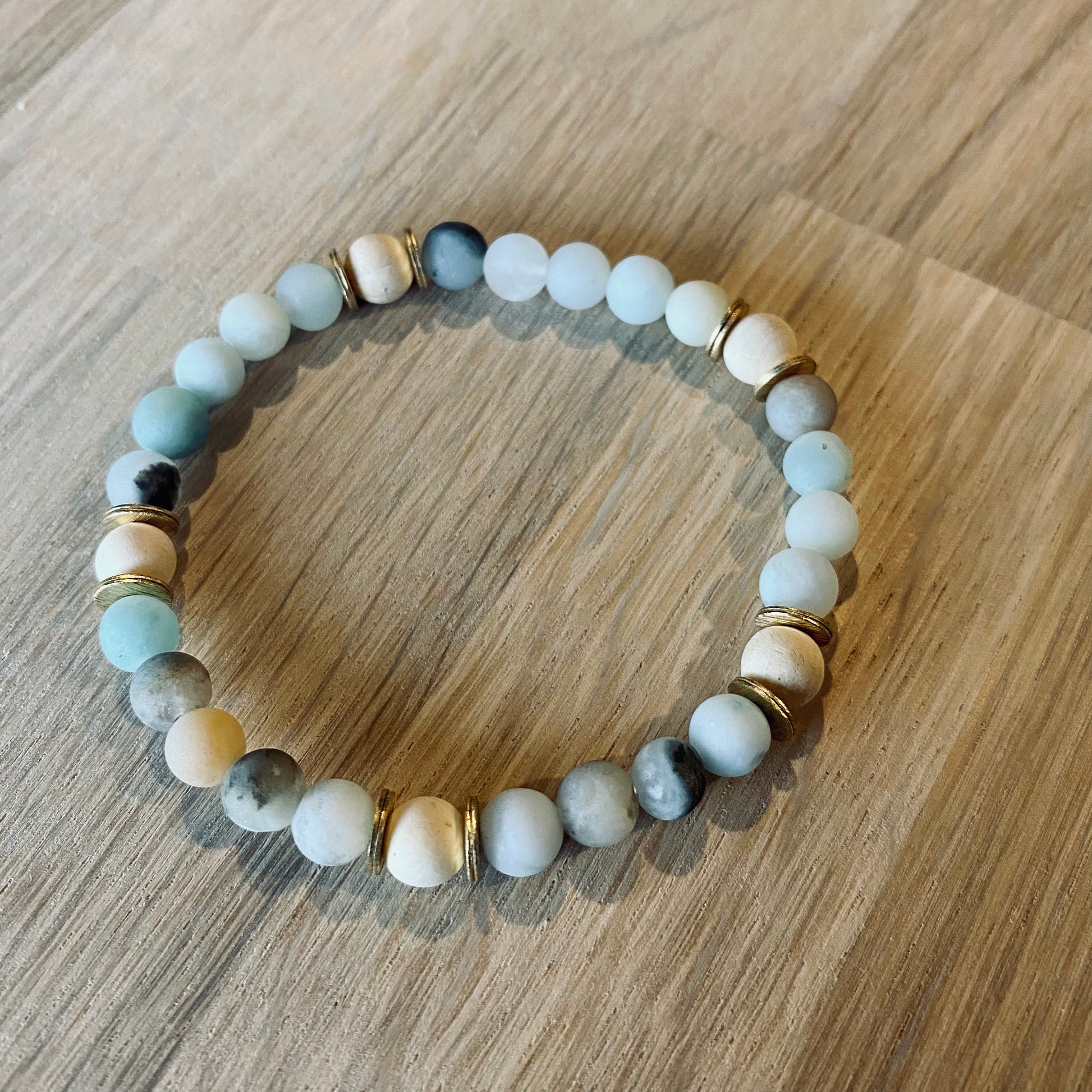 Amazonite aroma bracelet/diffuser bracelet made from 6mm amazonite & natural white wood beads with brass heishi disc embellishments. Laid flat on wood grain surface. 