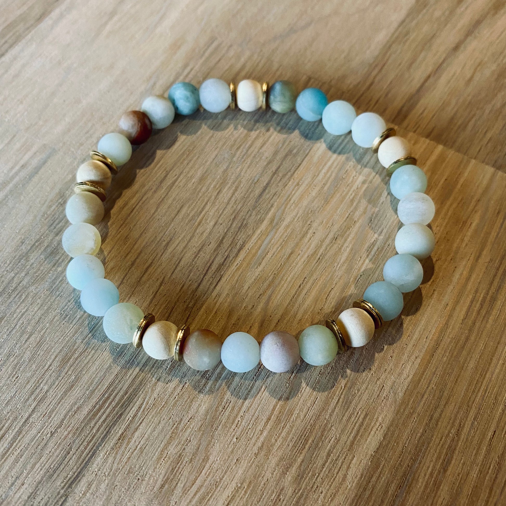 Amazonite aroma bracelet/diffuser bracelet made from 6mm amazonite & natural white wood beads with brass heishi disc embellishments. Laid flat on wood grain surface. 