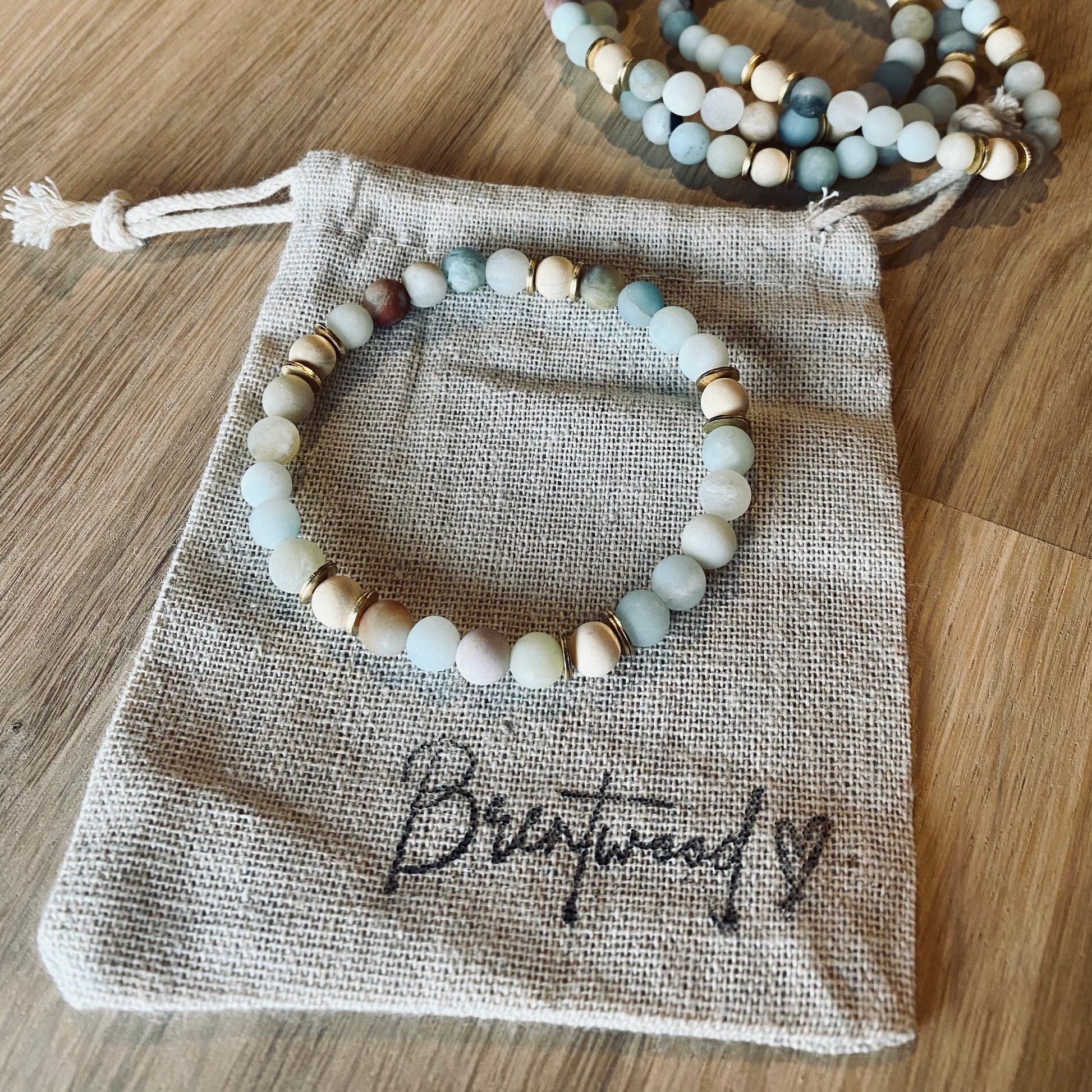 Amazonite aroma bracelet/diffuser bracelet made from 6mm amazonite & natural white wood beads with brass heishi disc embellishments. Laid on cloth pouch/drawstring bag stamped with “Brentwood” and a heart.