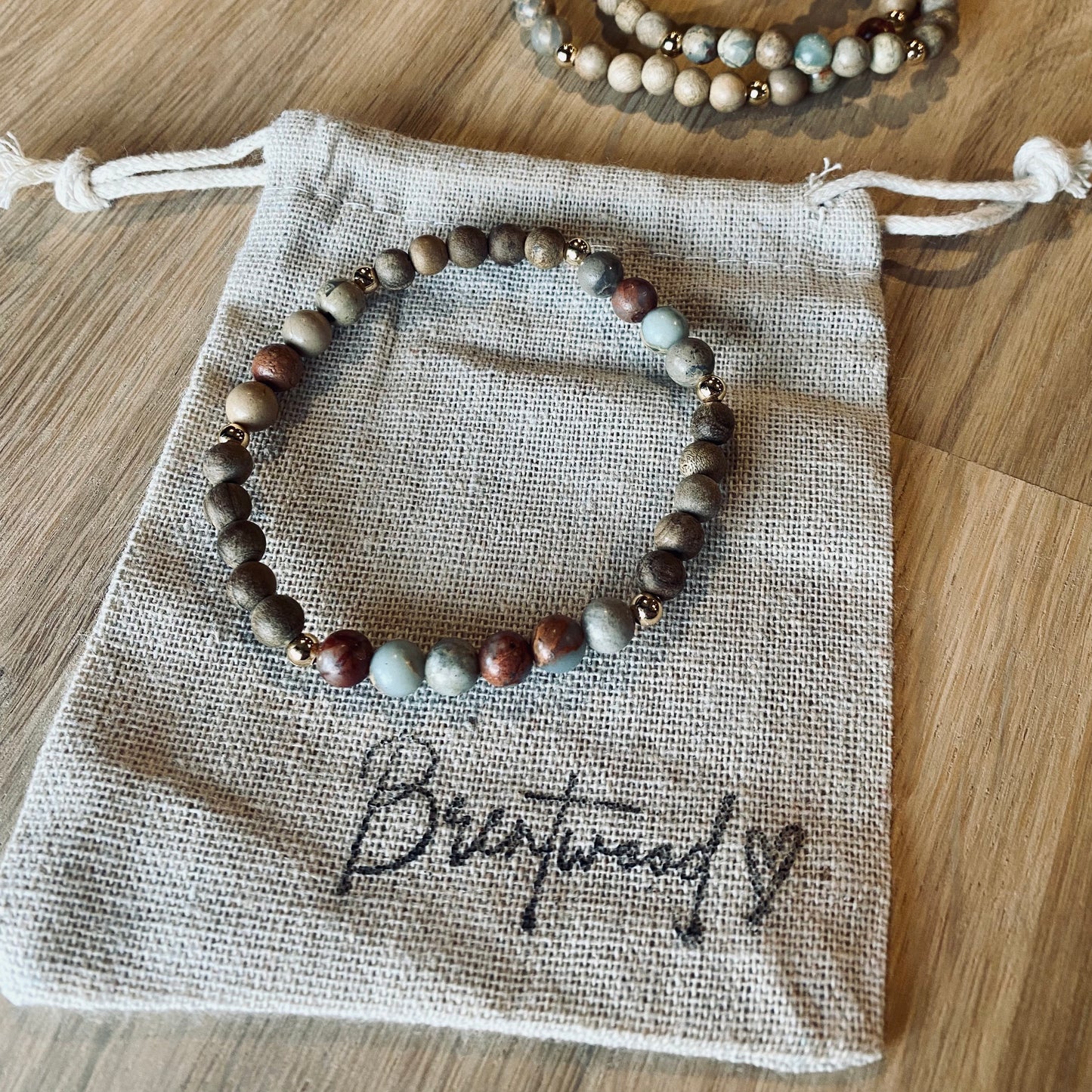 Aqua Terra Jasper aroma bracelet/diffuser bracelet made from 6mm Aqua Terra Jasper & natural burly wood beads with 18k gold plated embellishments. Laid on cloth pouch/drawstring bag stamped with “Brentwood” and a heart. 