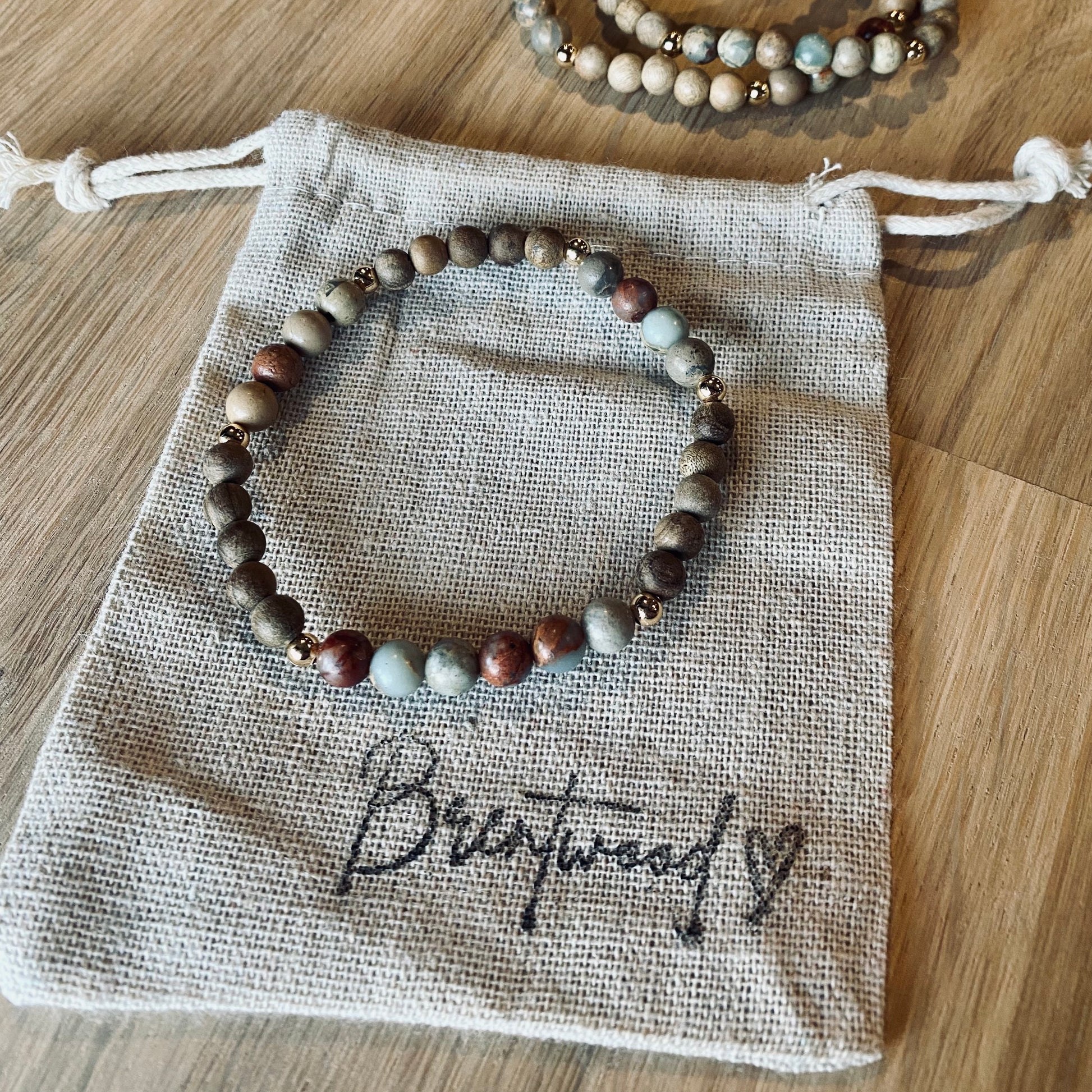 Aqua Terra Jasper aroma bracelet/diffuser bracelet made from 6mm Aqua Terra Jasper & natural burly wood beads with 18k gold plated embellishments. Laid on cloth pouch/drawstring bag stamped with “Brentwood” and a heart. 