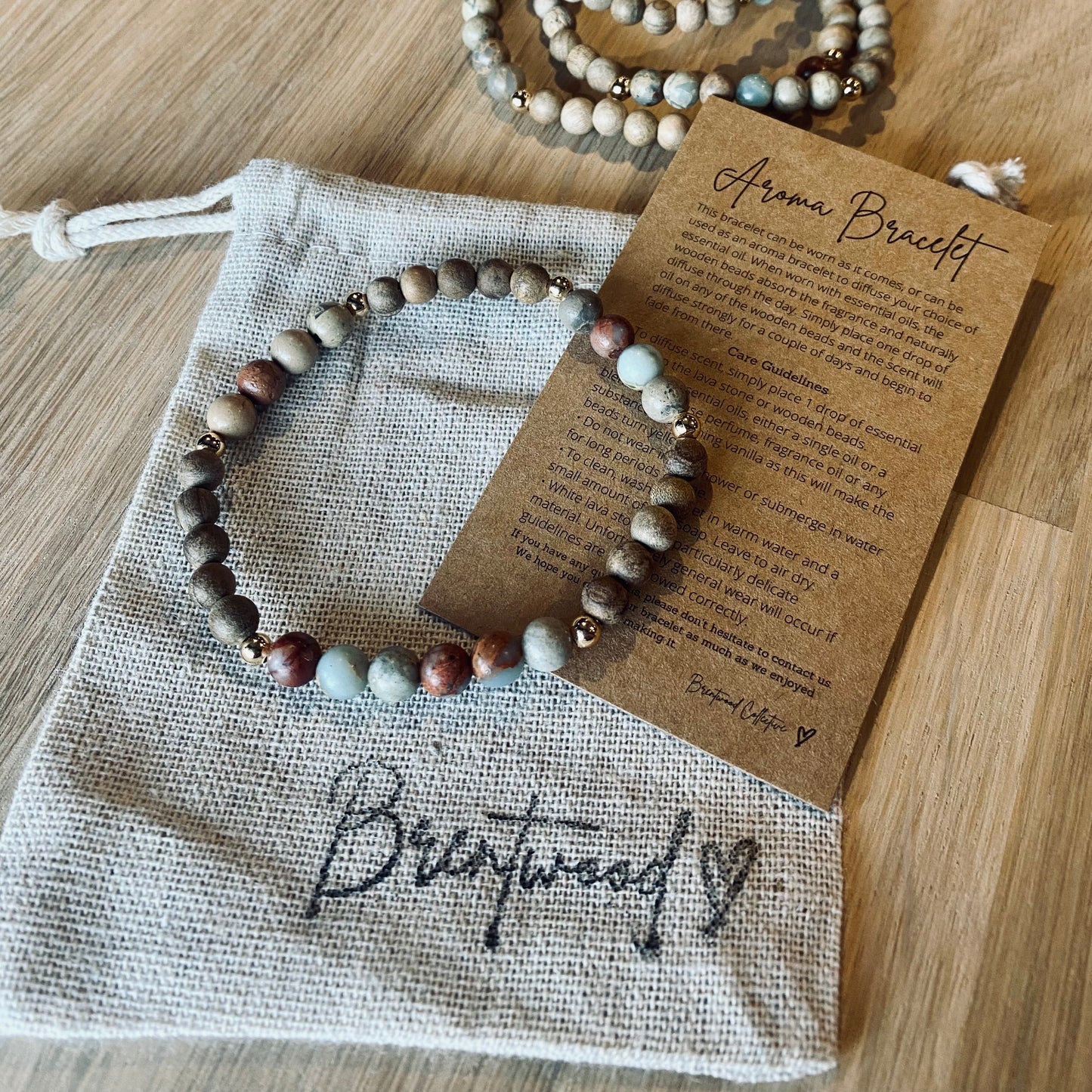 Aqua Terra Jasper aroma bracelet/diffuser bracelet made from 6mm Aqua Terra Jasper & natural burly wood beads with 18k gold plated embellishments. Laid on cloth pouch/drawstring bag stamped with “Brentwood” and an aroma bracelet information and care card on kraft brown card. 
