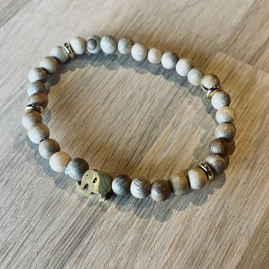 Gold Elephant aroma bracelet/diffuser bracelet made from 6mm burly wood beads beads with gold lucky elephant charm and gold disc embellishments. Laid flat on wood grain surface. 