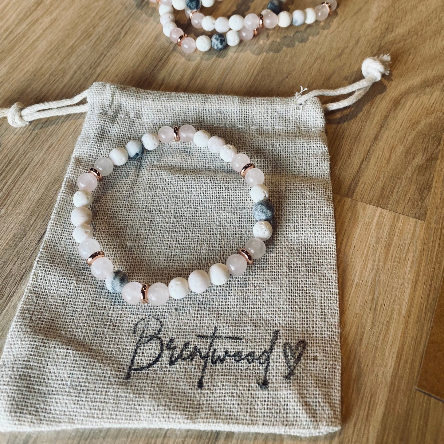 Pink Zebra Jasper Aroma Bracelet - 6mm beaded diffuser bracelet made from a pattern of pink zebra jasper, rose quartz, white lava stone & rose gold disc embellishments. Laid on cloth pouch/drawstring bag stamped with “Brentwood” and a heart.