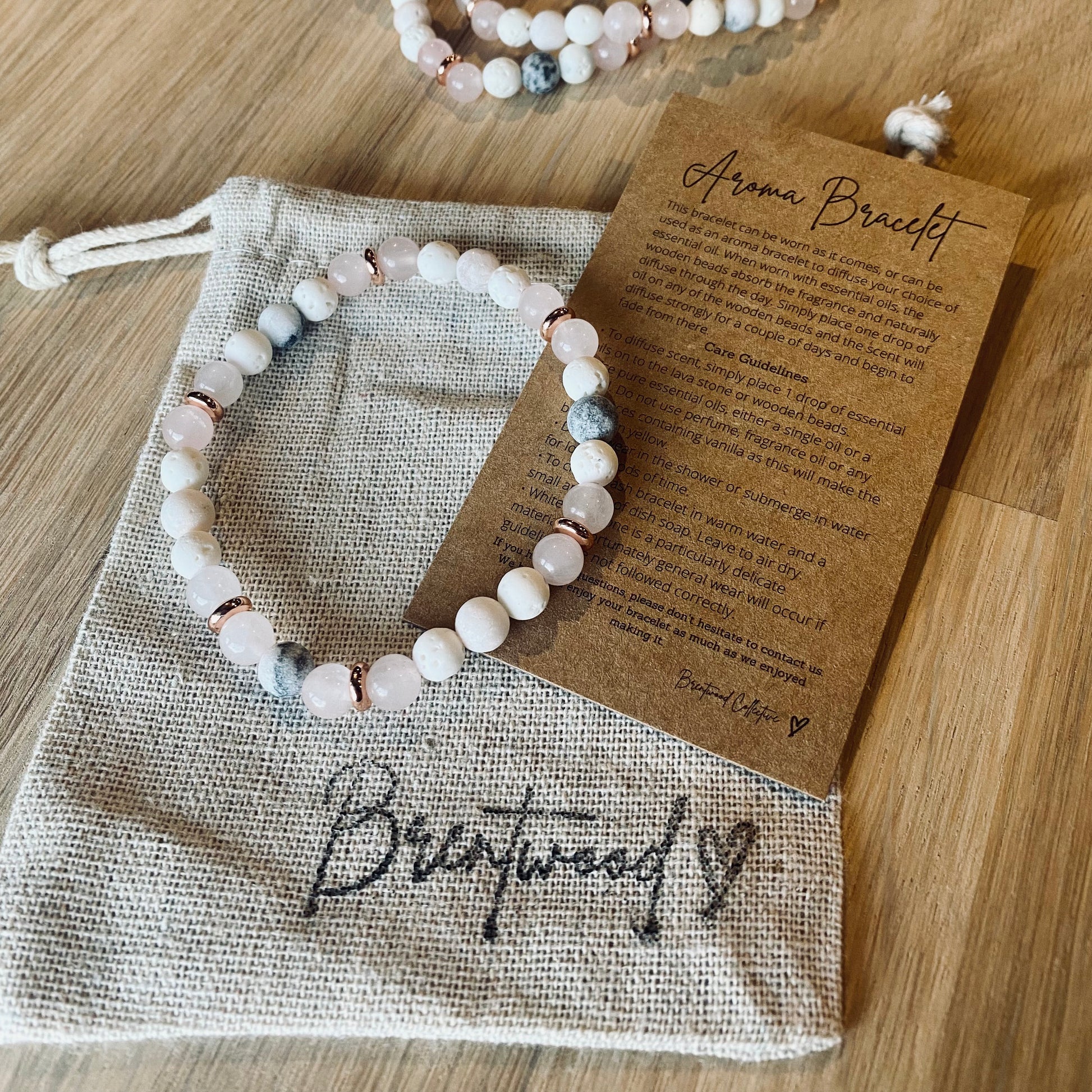 Pink Zebra Jasper Aroma Bracelet - 6mm beaded diffuser bracelet made from a pattern of pink zebra jasper, rose quartz, white lava stone & rose gold disc embellishments. Laid on cloth pouch/drawstring bag stamped with “Brentwood” and an aroma bracelet information and care card on kraft brown card.