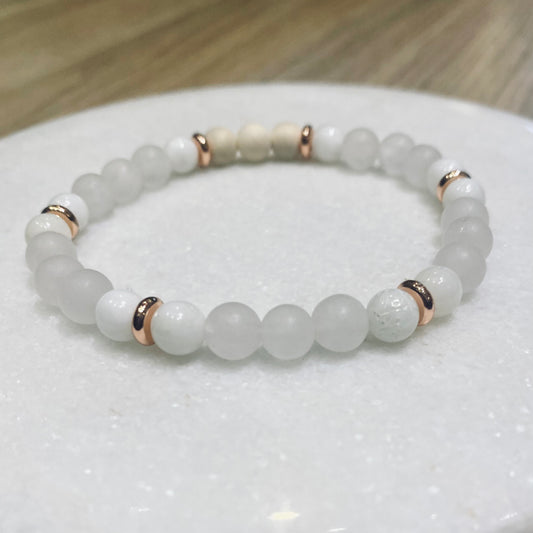 Rose Quartz Shell Aroma Bracelet - 6mm beaded diffuser bracelet made from rose quartz, natural shell & white natural wooden beads with rose gold discs as embellishments. Laid flat on white quartz round surface.