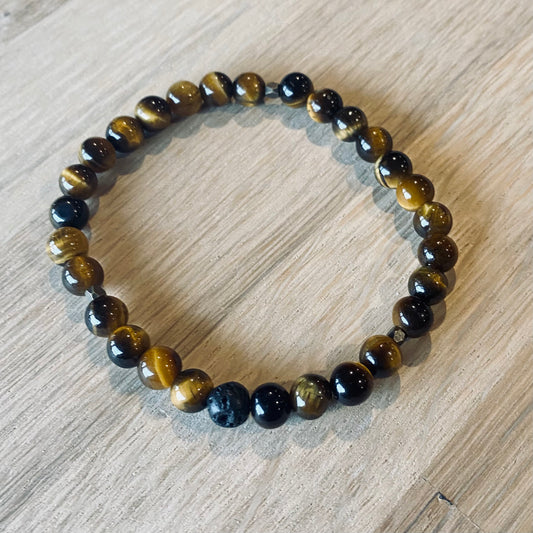 Tiger Eye 6 Aroma Bracelet - 6mm beaded diffuser bracelet made from natural tiger eye gemstone & a single black lava stone bead with antiqued gold faceted embellishments.  Laid flat on wood grain surface. 