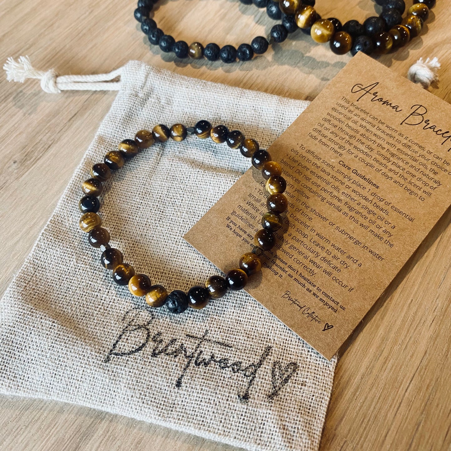 Tiger Eye 6 Aroma Bracelet - 6mm beaded diffuser bracelet made from natural tiger eye gemstone & a single black lava stone bead with antiqued gold faceted embellishments.  Laid on cloth pouch/drawstring bag stamped with “Brentwood” and an aroma bracelet information and care card on kraft brown card.