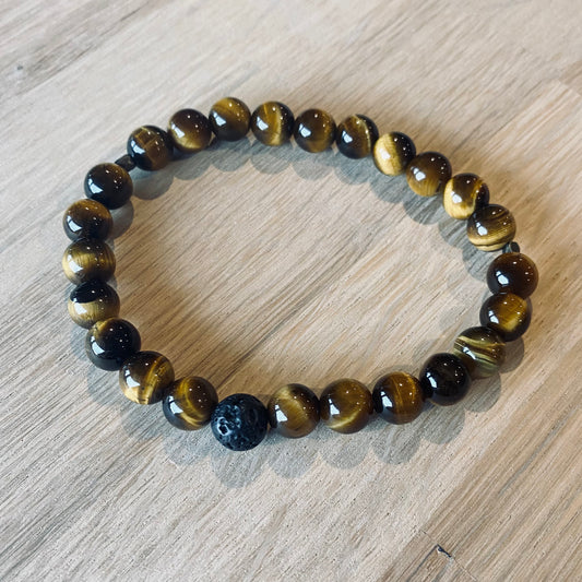 Tiger Eye 8 Aroma Bracelet - 8mm beaded diffuser bracelet made from natural tiger eye gemstone & a single black lava stone bead with antiqued gold faceted embellishments.   Laid flat on wood grain surface. 